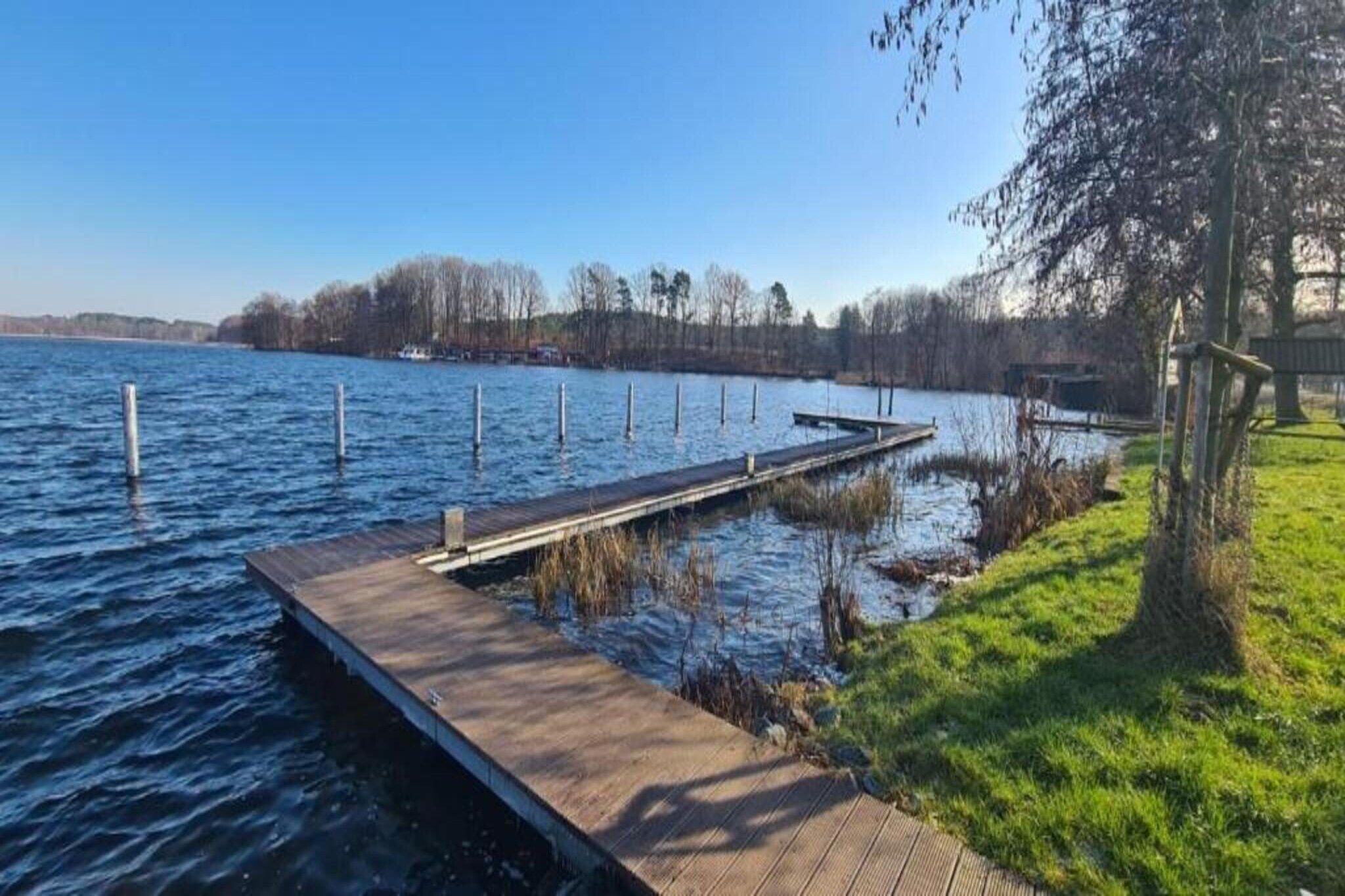 A wooden dock extending into a calm body of water, surrounded by grassy areas and trees.