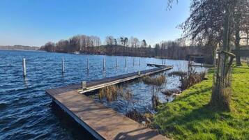 A wooden dock extending into a calm body of water, surrounded by grassy areas and trees.