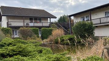 Ein Wohngebäude mit Balkon, Treppe und Teich mit Vegetation.