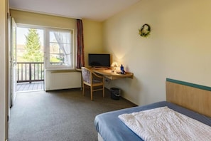 Ein Hotelzimmer mit einem Bett, einem Schreibtisch mit Computer, einem Stuhl, einem Fenster mit Vorhängen und Blick ins Freie.