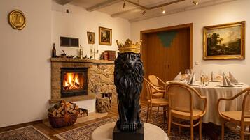 Ein Zimmer mit Kamin, einer Löwenstatue, Korbstühlen, einem Esstisch für vier Personen und einem Gemälde an der Wand.