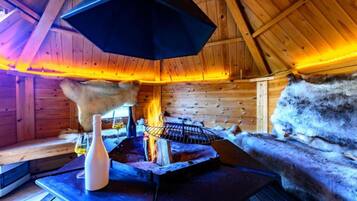 L’intérieur d’un chalet en bois, avec une cheminée, des murs recouverts de fourrure et une table sur laquelle se trouvent une bouteille et des verres.