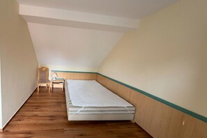 A small, triangular attic bedroom with a wooden floor, a single bed, a nightstand, and a chair.