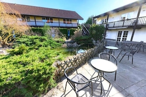 Ein Innenhof mit einem kleinen Teich, Sitzgelegenheiten im Freien und einem Gebäude mit einem Balkon.