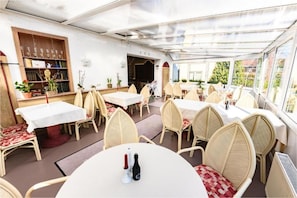 Ein Restaurant mit runden Tischen und Korbstühlen, einer Bar und Blick durch große Fenster.