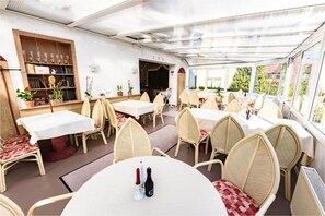 Ein Essbereich mit runden Tischen, Korbstühlen, einem Bücherregal und einem Fernseher.