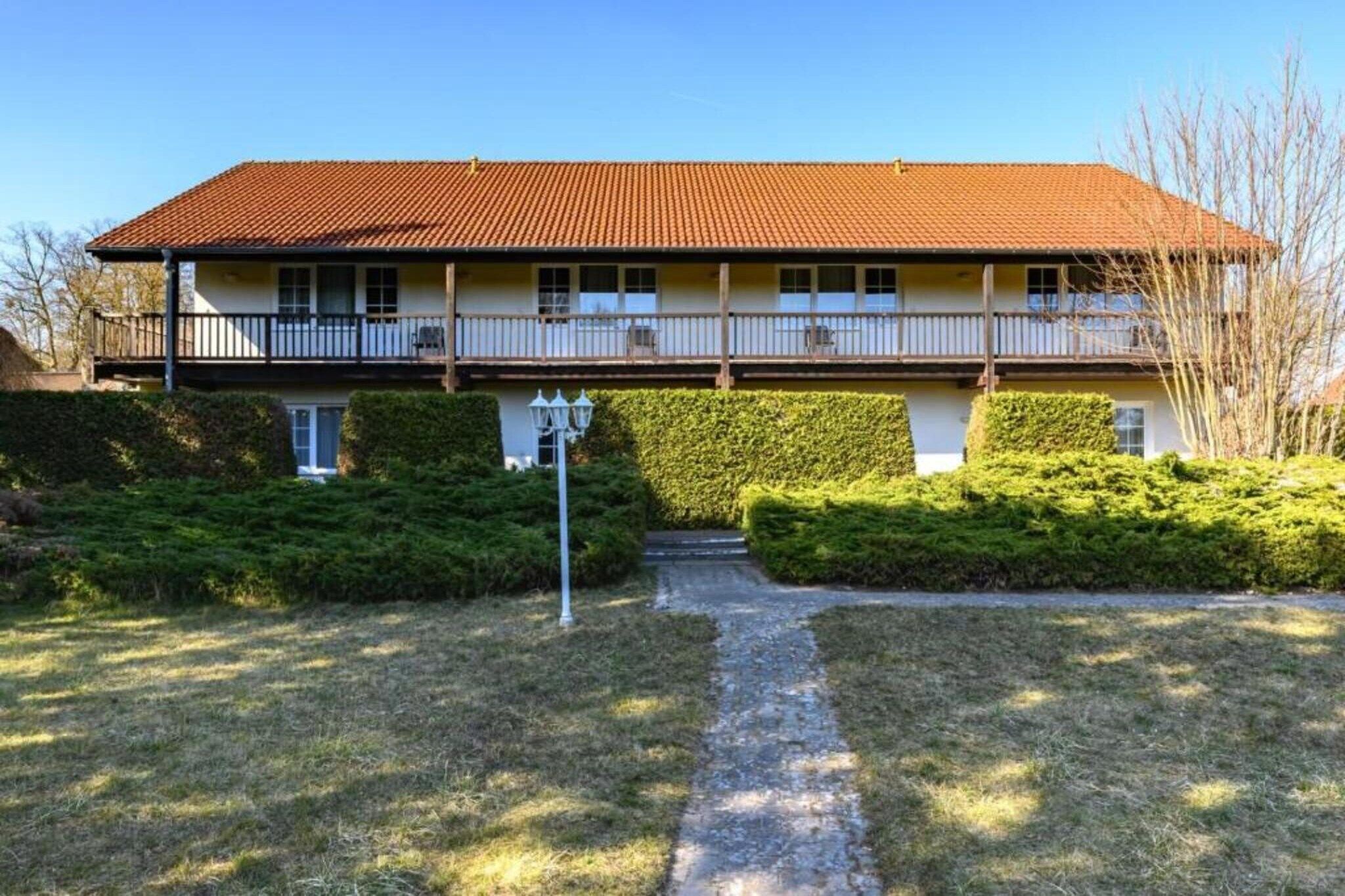 Un bâtiment à deux étages, doté d’un toit recouvert de tuiles rouges, d’un balcon à l’étage supérieur et d’un chemin menant à l’entrée.