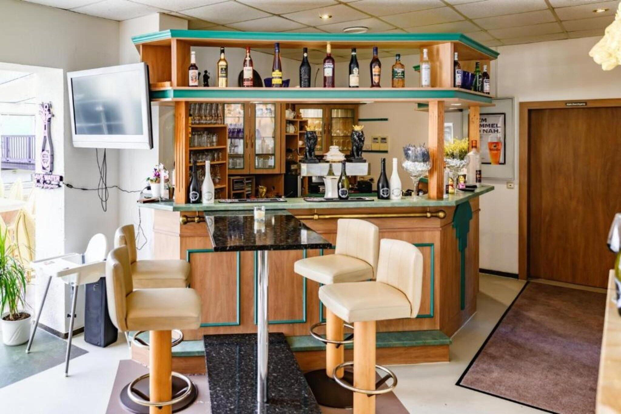 Un espace bar avec des tabourets, un comptoir et des étagères remplies de bouteilles.