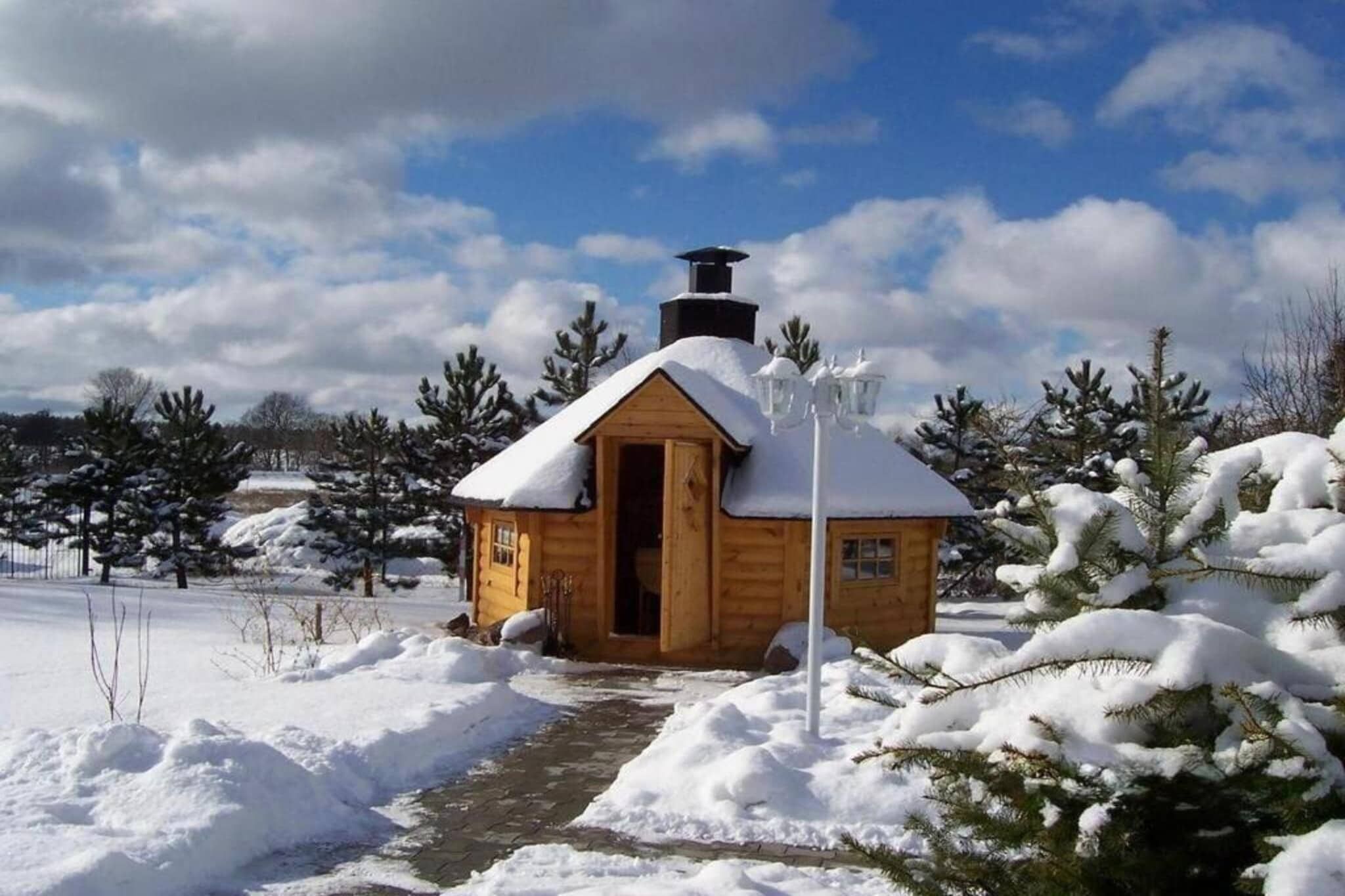 Une cabane en bois, dont le toit est recouvert de neige, avec une cheminée et un sentier menant à l’entrée.