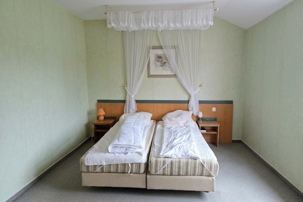 A double bed with white linens, a wooden headboard, two bedside tables with lamps, and a canopy bed with sheer curtains.