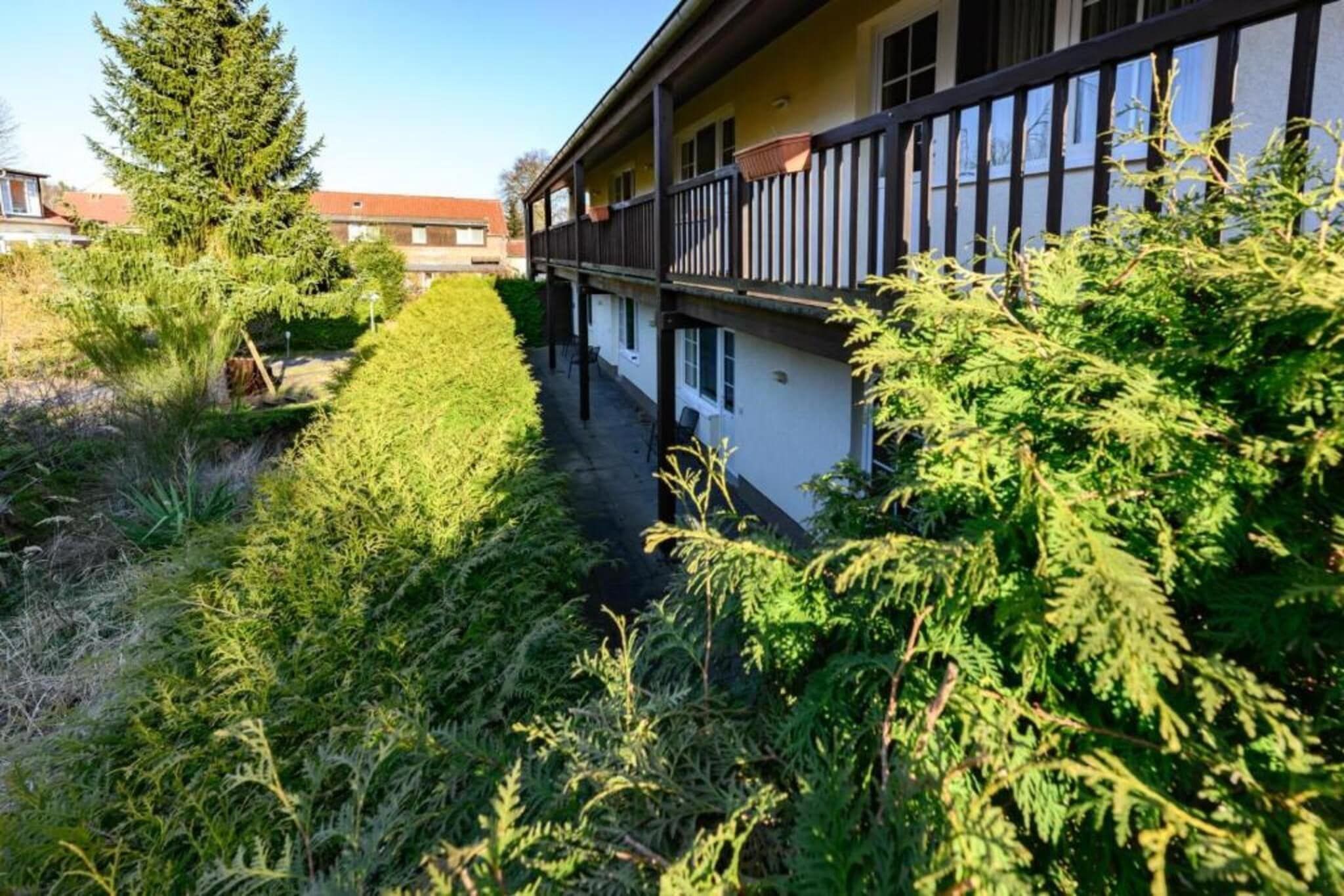 A building with a balcony, surrounded by dense greenery and a clear sky.