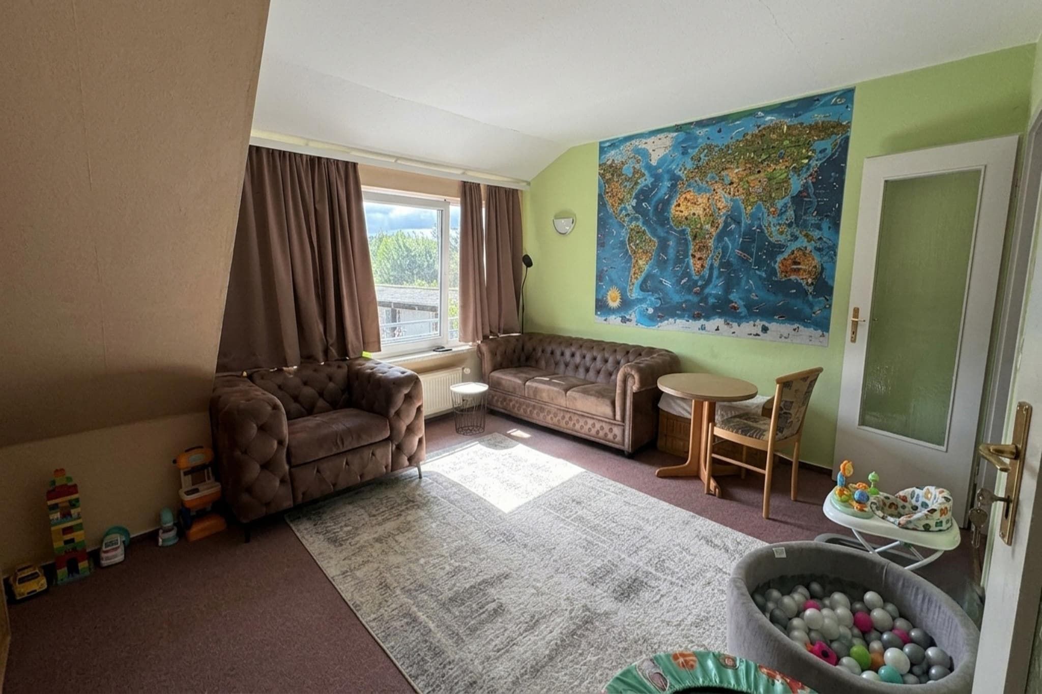 Ein Wohnzimmer mit einer Couch, einem kleinen Tisch, Wandkunst mit einer Weltkugel und einem Spielbereich mit Spielzeug.
