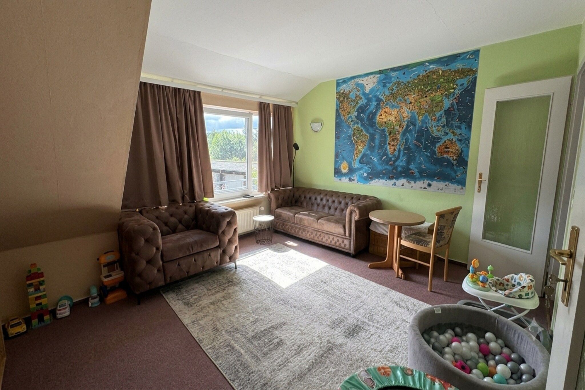 Un salon comprenant un canapé, un fauteuil, une petite table, une décoration murale représentant un globe terrestre et un espace de rangement pour les jouets.