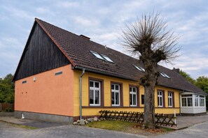 Un edificio de dos plantas con techo inclinado, ventanas dormer y un árbol en la fachada.