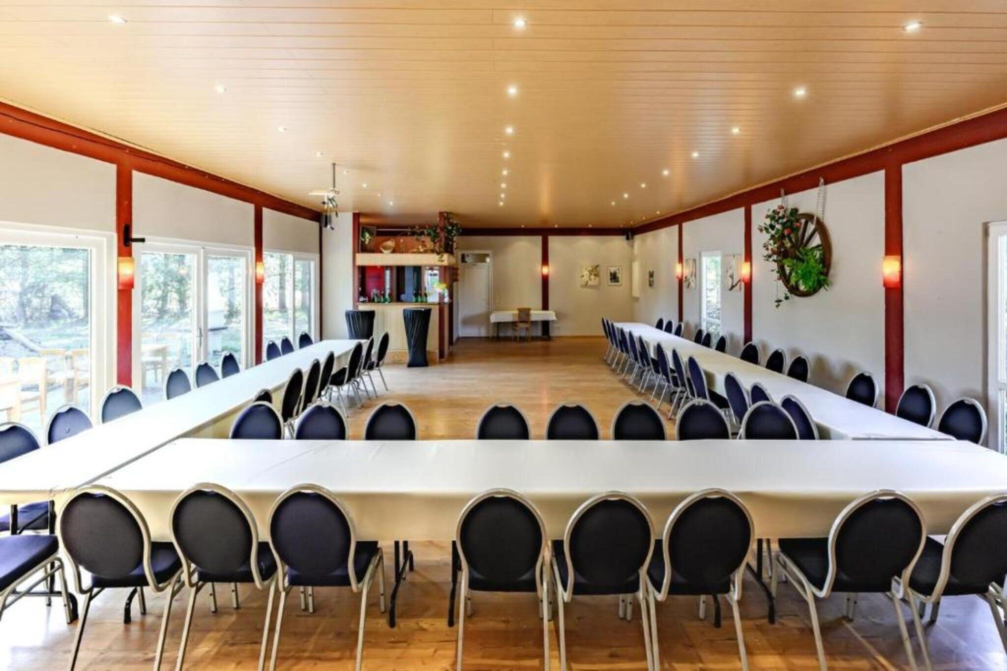 Une salle de conférence avec une longue table et des chaises, un plancher en bois et un coin cuisine à l’arrière-plan.