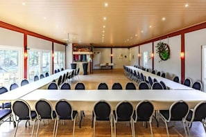 Un salón de conferencias con una larga mesa y sillas, pisos de madera y una cocina al fondo.