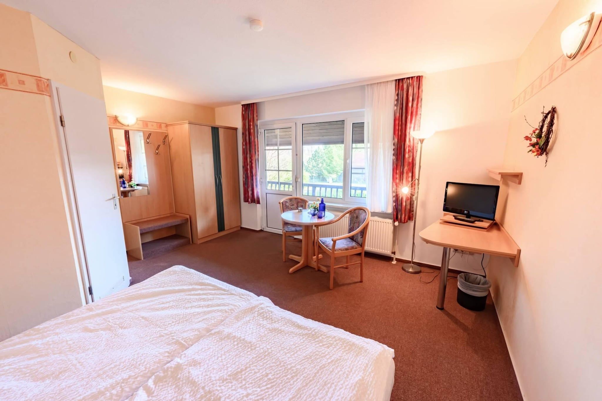 Ein Hotelzimmer mit Bett, Schreibtisch mit Fernseher, Stuhl, kleinem Tisch und einem Fenster mit Vorhängen.