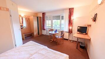 Ein Hotelzimmer mit Bett, Schreibtisch mit Fernseher, Stuhl, kleinem Tisch und einem Fenster mit Vorhängen.