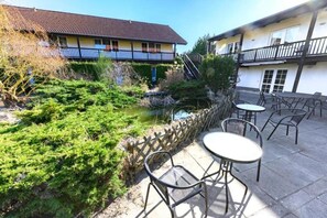 Ein Innenhof mit einem kleinen Teich, Sitzgelegenheiten im Freien und einem Gebäude mit einem Balkon.
