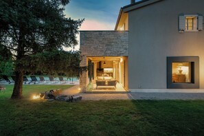 Uma casa moderna com fachada de pedra, entrada bem iluminada e área de piscina ao fundo.