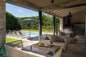 Espaço ao ar livre coberto com piscina, espregui çadeiras, mesa de jantar com café da manhã e área de cozinha.