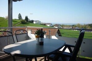 A terrace with a table and chairs, a bottle of wine, and a view of houses and greenery. - Bernhard Winery Type A (Daisendorf)