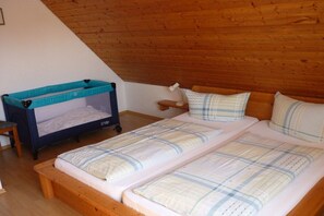 A room with a sloped ceiling, a bunk bed with a blue mattress, a bedside table with a lamp, and a small shelf. - Bernhard Winery Type A (Daisendorf)