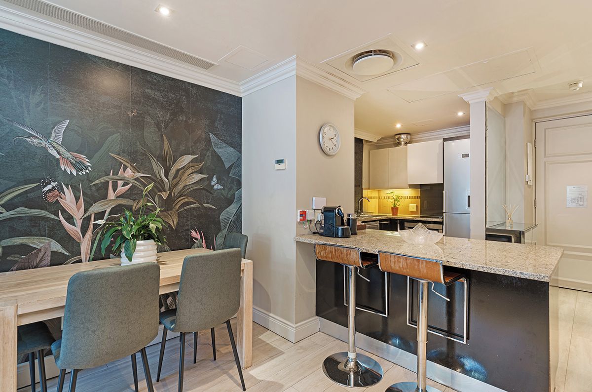 A modern kitchen with a bar area, a dining table with chairs, and a large mural on the wall.