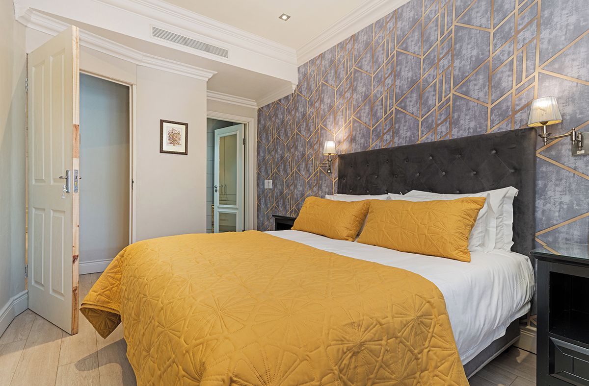 Quarto de hotel com cama, mesa de cabeceira, luminária na parede e porta.