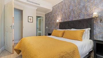 Quarto de hotel com cama, mesa de cabeceira, luminária na parede e porta.