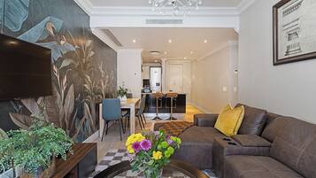 Ein Wohnzimmer mit Sofa, Couchtisch und einer Vase mit Blumen. Im Hintergrund ist eine Essecke mit Stühlen und einem Tisch zu sehen.