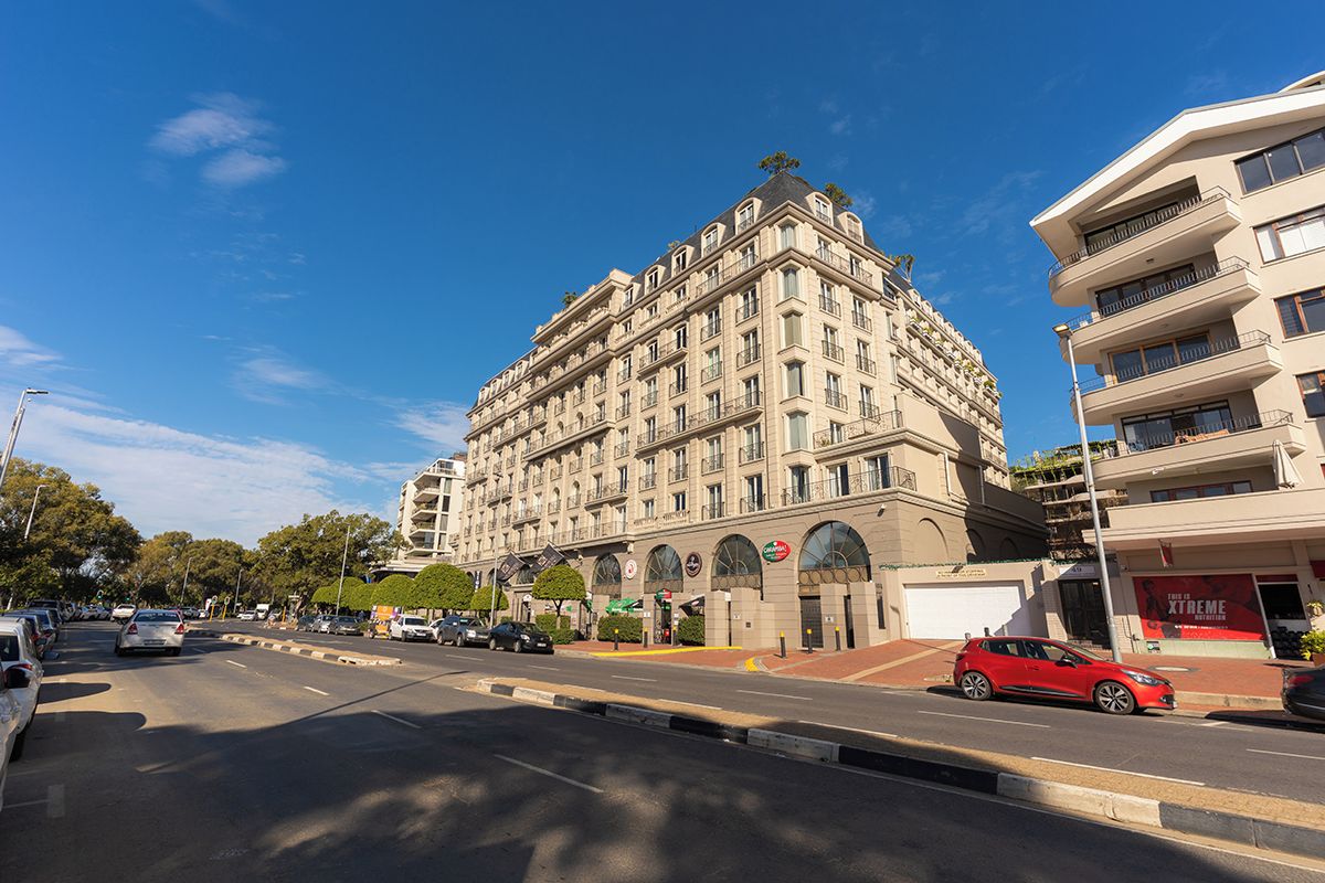 Um hotel de vários andares com design arquitetônico clássico, destacando uma entrada de canto e um amplo estacionamento em frente.