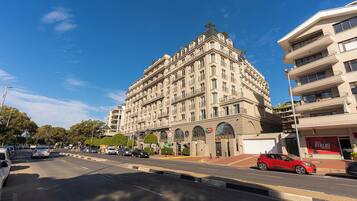 Um hotel de vários andares com design arquitetônico clássico, destacando uma entrada de canto e um amplo estacionamento em frente.