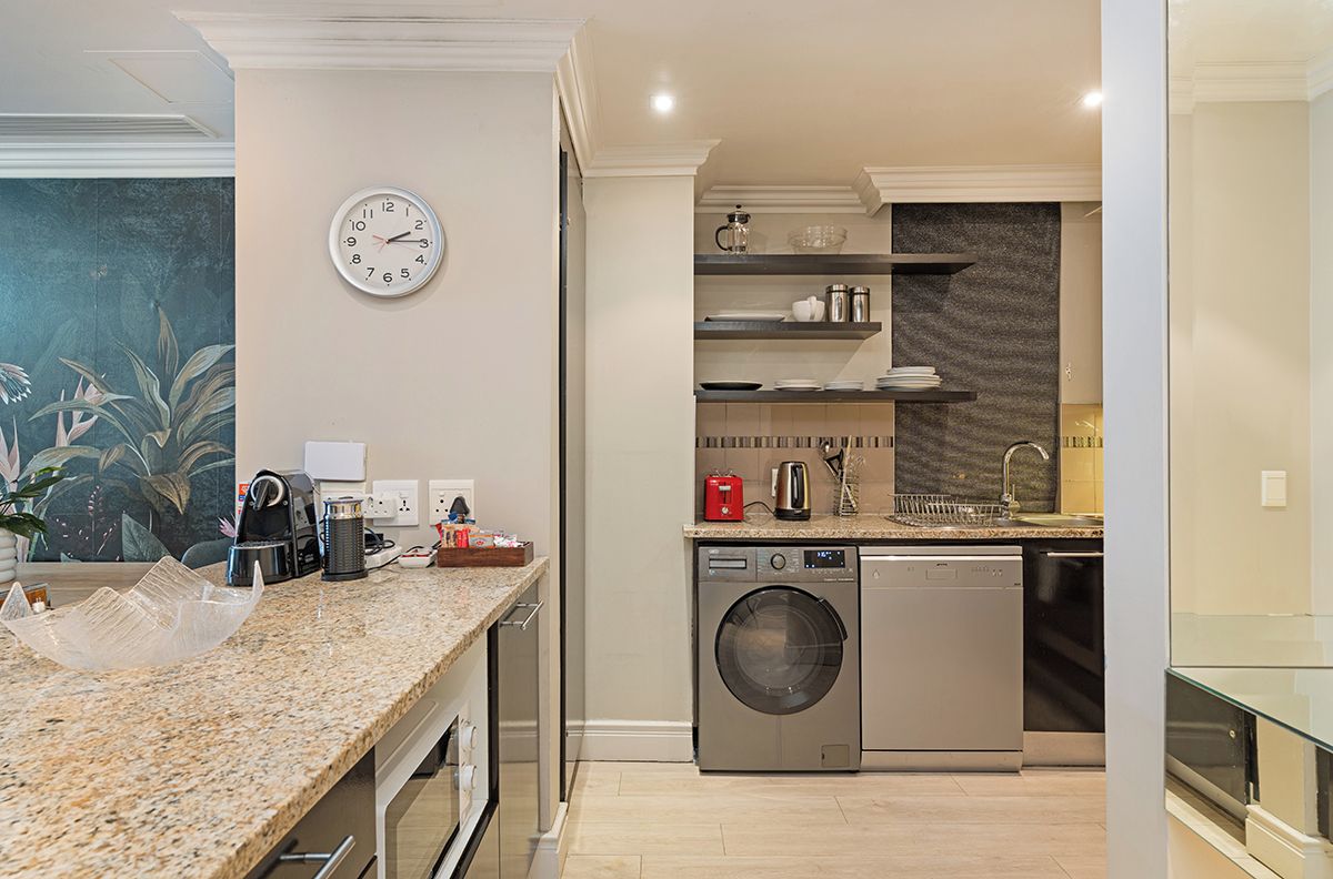 A modern kitchen with a built-in washer and dryer, granite countertops, and a clock on the wall.