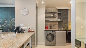 A modern kitchen with a built-in washer and dryer, granite countertops, and a clock on the wall.