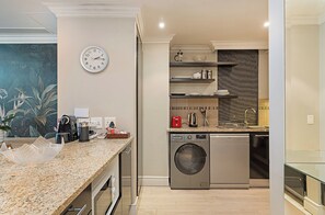 A modern kitchen with a built-in washer and dryer, granite countertops, and a clock on the wall.