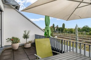 Ein Balkon mit einem grünen Stuhl, zwei Topfpflanzen und einem großen Sonnenschirm.