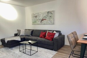 Uma sala de estar moderna com um sofá seccional, uma mesa de centro e uma área de jantar com mesa e cadeiras.