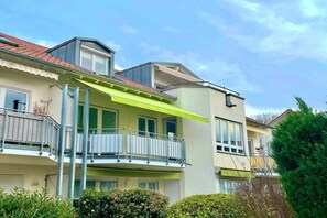 Un immeuble résidentiel de deux étages doté d’un balcon, d’un auvent vert et d’un toit recouvert de tuiles rouges.