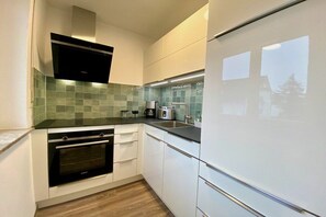 A modern kitchen with white cabinets, a black oven, and a green-tiled backsplash. - Holiday apartment with 1 bedroom (Langenargen)