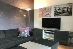 A modern living room with a sofa, a coffee table, a TV, and artwork on the wall. - ||---------------------------------at the hop garden---------------------|| (Lindau)