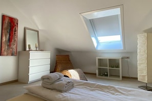 A bedroom with a skylight, a white dresser, a bedside table with candles, and a painting on the wall. - ||---------------------------------at the hop garden---------------------|| (Lindau)