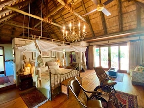 A room with a bed, a chair, a table, and a ceiling fan.