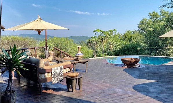 A wooden deck with outdoor furniture, a pool, and a view of the surrounding landscape.