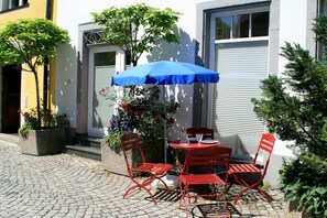 An outdoor patio with a red metal table and chairs, a blue umbrella, and potted plants. - Holiday apartment LiLi 10 (Lindau)