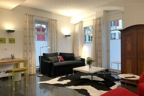 A living room with a black sofa, a white coffee table, a cowhide rug, a wooden cabinet, and a small table with a chair. - Holiday apartment LiLi 10 (Lindau)