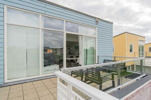 A modern building with large sliding glass doors, a balcony with a glass railing, and a tiled patio area. - Holiday home with 1 bedroom (Oude-Tonge)