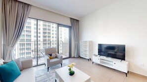 Ein modernes Wohnzimmer mit Sofa, Sessel, Fernseher und einem Balkon mit Blick auf hohe Gebäude.