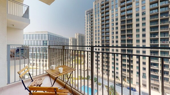 A balcony with a wooden table and chairs, overlooking a residential area with high-rise buildings. - Homey 2 Bed l Dubai Hills Mall within Community (Dubai Hills)
