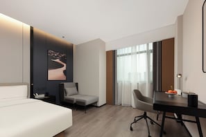 Et moderne hotelværelse med en seng, to stole, et skrivebord og et stort vindue med gardiner.